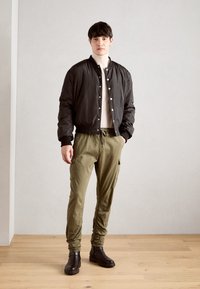 Zwarte bomberjack, crèmekleurige coltrui, olijfgroene cargo pants, bruine enkellaarsjes. Jack heeft drukknoopsluiting, de broek heeft verstelbare boorden en zakken.