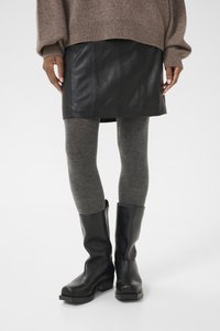 Minifalda de cuero negro combinada con leggings texturizados grises y botas negras hasta la rodilla. El suéter es marrón con puños y dobladillo acanalados.