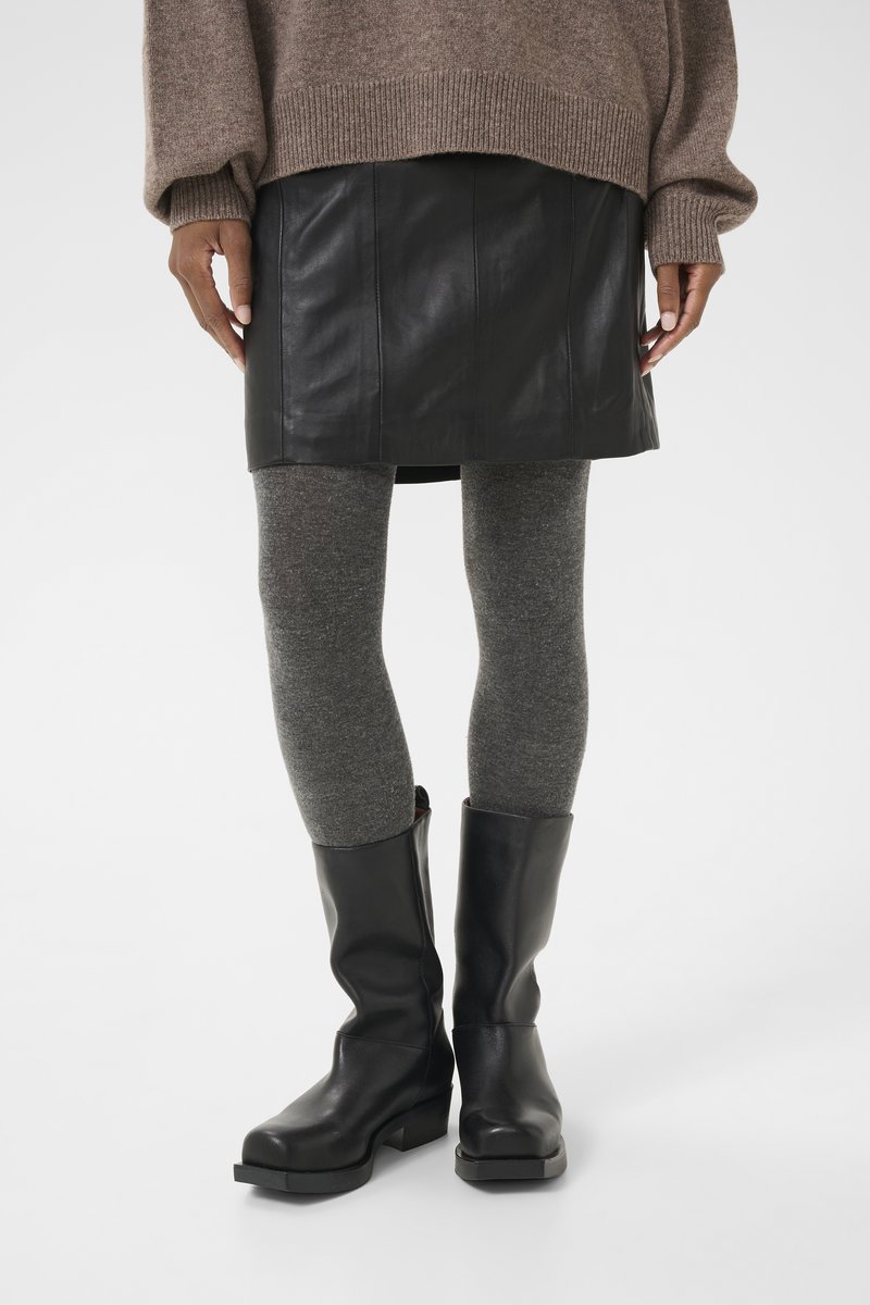 Minifalda de cuero negro combinada con leggings texturizados grises y botas negras hasta la rodilla. El suéter es marrón con puños y dobladillo acanalados.