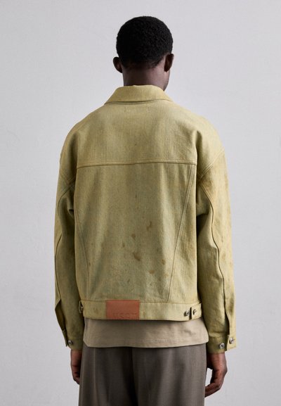 Light green denim jacket with a slightly textured surface, featuring a tan leather patch at the back and button accents on the cuffs.