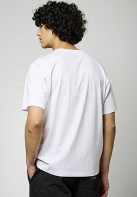 T-shirt en coton blanc à manches courtes, coupe décontractée et col rond. Couture visible et petite étiquette dans le bas du dos.