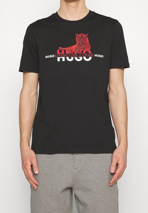 Svart bomullströja med ett tigermotiv i rött och vit text "HUGO LIVING LIKE A TIGER." Korta ärmar och rundad halsringning.