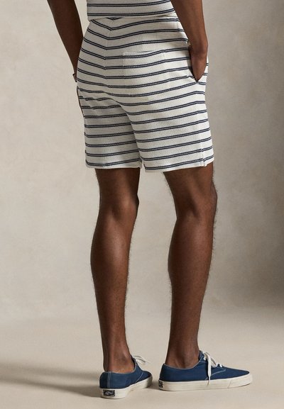 Férfi csíkos rövidnadrág fehér és tengerészkék színekben. Könnyű anyagból készült, oldalán zsebekkel és egyenes szabással. Kék vászoncipővel párosítva.