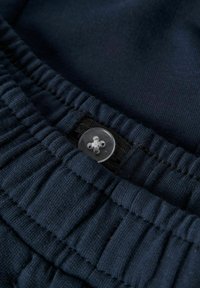 Tumesinise värvusega riietus tekstuuriga kangast, millel on soonikkoe vöökoht ja selge plastnupp nelja auguga disainiga.