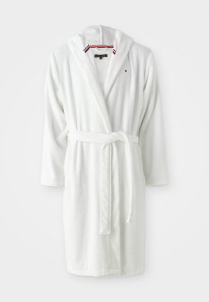 Λευκή ρόμπα μπάνιου από μαλακό στερεό ύφασμα, με κουκούλα, μακριά μανίκια και ζώνη που δένει στη μέση. Διαθέτει διακοσμητική ρίγα στον λαιμό.