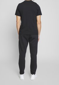 Svart bomullströja med korta ärmar, kombinerad med svarta träningsbyxor. Modellen bär vita sneakers, sedd från baksidan.