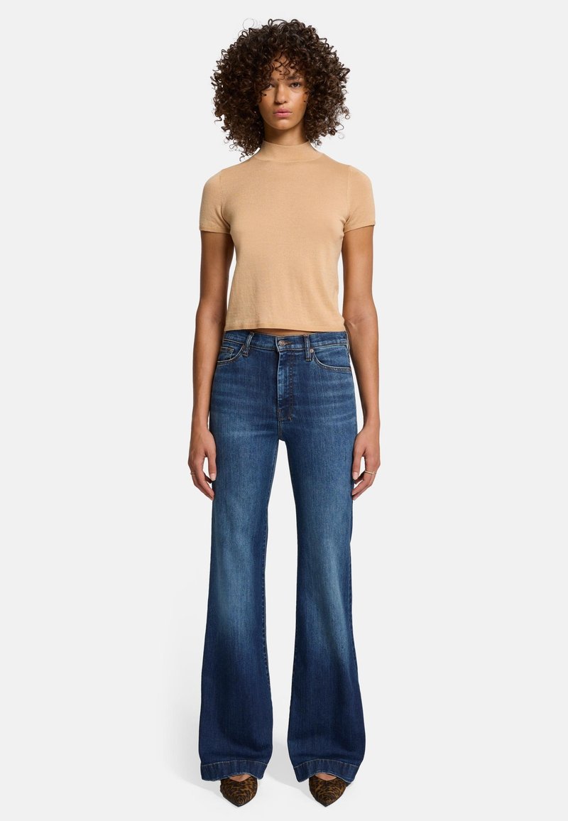 Beige fitted short-sleeve top paired with high-waisted, wide-leg dark blue denim jeans with a faded texture and a slight flare at the hem.