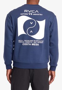Sweatshirt bleu marine avec poignets et ourlet côtelés, arborant un grand motif graphique blanc au dos incluant du texte et des motifs circulaires.
