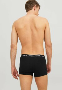 Schwarze Baumwoll-Boxershorts mit einem weißen "JACK & JONES"-Logo-Hosenbund, im taillierten Design. Sichtbare Haut auf dem Rücken des Modells.