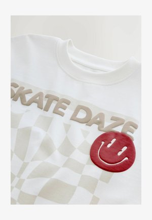 Weißes Sweatshirt mit 3D-beigem Schriftzug "SKATE DAZE", karierter Musterung und einem roten Smiley-Patch auf der Vorderseite, weiche Textur.