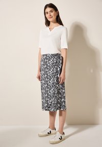 Top bianco a maniche corte con scollatura a V, abbinato a una lunga gonna nera e bianca con motivo, completato da sneaker bianche con accenti neri.