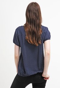 Camicia blu navy a maniche corte con un piccolo motivo a pois bianchi, dalla vestibilità comoda e orlo arricciato per un tocco di texture in più.