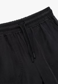 Pantalones de chándal negros con una superficie texturizada, cinturilla elástica y cordón ajustable. Cuenta con bolsillos laterales y detalles de costura.