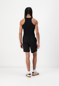 Top aderente nero abbinato a pantaloni corti neri con vita elastica. Le calzature sono sneakers bianche con dettagli neri e una suola color gomma.