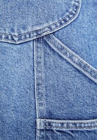 Light blue denim fabric featuring visible stitching, a curved pocket seam, and a smooth, textured surface with a classic wash effect.