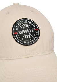 Beige baseball cap made of cotton with a black circular patch featuring "CAMP DAVID," numbers, and "PREMIUM QUALITY" text in white.