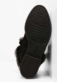 Bottine en daim noir avec semelle en caoutchouc texturée, détails en fausse fourrure et design à bout arrondi. Comprend un logo Gabor sur la semelle extérieure.
