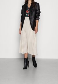 Svart skinnblazer, blommönstrad topp, plisserad krämfärgad midikjol och svarta klackade ankelboots. Släta texturer och skräddarsydd passform.