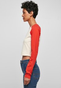 Kurz geschnittenes Langarmshirt in kontrastierenden Rot- und Cremetönen, aus weicher Baumwolle gefertigt, mit rundem Ausschnitt und taillierten Ärmeln.