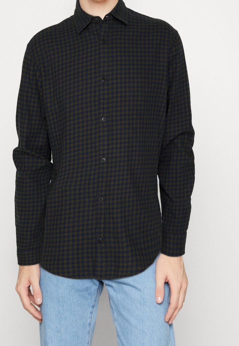 Camicia button-up a quadri verde scuro e blu navy con maniche lunghe, colletto e bottoni neri. Indossata con jeans azzurri chiari.