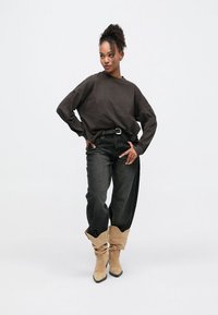 Σκούρο καφέ φαρδύ φούτερ, μαύρα φαρδιά τζιν και μπεζ χαλαρά μπότες. Το σύνολο έχει άνετη εφαρμογή και casual στιλ.