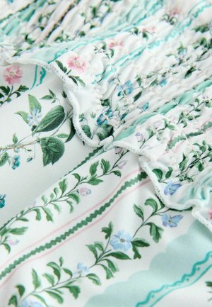 Tessuto con motivo floreale dai colori pastello, caratterizzato da dettagli arricciati e bordi volant. Foglie verdi e fiori blu su sfondo bianco.