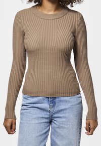 Haut marron à manches longues côtelées avec un col rond, fabriqué à partir d'un matériau texturé. Associé à un jean taille haute bleu clair.