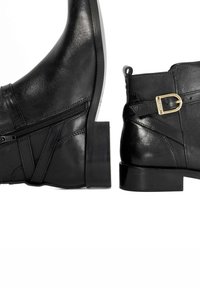Black leather ankle boots with a pointed toe, side zipper closure, and a decorative strap with a gold buckle on the heel.