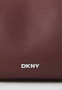 Burgundi színű, textúrázott bőr pénztárca ezüst DKNY logóval az alján, minimalista designnal és sima felülettel.