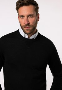 Maglione nero a maglia con scollatura rotonda e dettagli a coste. Presenta una texture liscia e un sottile dettaglio a forma di V al colletto.