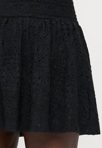 Zwarte rok met een getextureerd, geborduurd patroon en oogjesdetails. Uitlopende stijl met een gesmokte tailleband voor flexibiliteit.