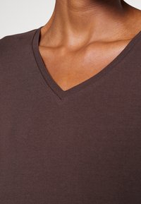 Braunes V-Ausschnitt-T-Shirt aus weicher Baumwolle, mit glatter Textur und lockerem Schnitt, mit an den Rändern sichtbaren kurzen Ärmeln.