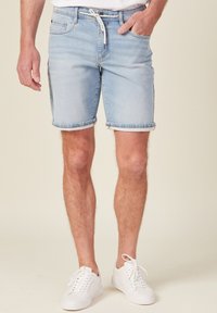 Ljusblå denimshorts med uppvikta fållar, med en dragsko i midjan och sidofickor, kombinerat med vita sneakers.