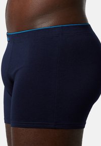 Boxer shorts di un blu scuro con una texture liscia, caratterizzati da una cintura contrastante di un blu chiaro e dettagli di cucitura minimi.