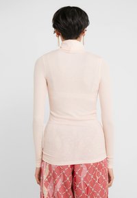 Helles rosa eng anliegendes Rollkragenoberteil aus gerippter Textur, mit langen Ärmeln und hohem Kragen, kombiniert mit gemusterten rosa Hosen.