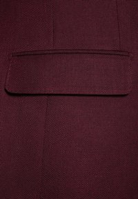 Bordowy materiał o teksturowanym splocie, z prostokątną klapką kieszeni przyszytą z jednej strony, o płaskiej i gładkiej powierzchni.