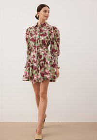 Kwiatowa sukienka w odcieniach zieleni z różowymi i burgundowymi wzorami, z bufiastymi rękawami, zapinana na guziki z przodu oraz z wcięciem w talii podkreślonym paskiem.