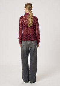 Lace top in burgundy with a diamond pattern, featuring long sheer sleeves and a collar, paired with high-waisted gray wide-leg jeans.