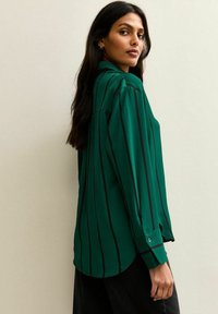 Groene gestreepte shirt met een kraagontwerp, lange mouwen, knopenaccenten en een zachte textuur, met verticale zwarte strepen.