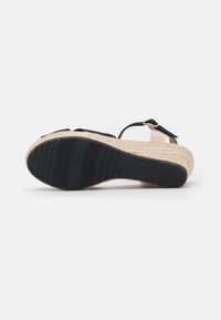 Kilklackssandal med en texturerad, vävd halmklack. Ovandelen har släta, marinblå tygremmar och en gummisula med grepplinjer.