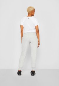 Hvid cropped T-shirt med et sort logo på ryggen, parret med lysegrå joggers og sorte sko. Blødt stof og afslappet pasform.