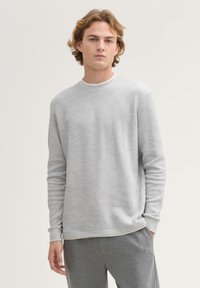 Grauer Pullover mit langen Ärmeln und Rundhalsausschnitt. Glatte Textur und einfaches Design. Getragen mit passenden grauen Hosen.