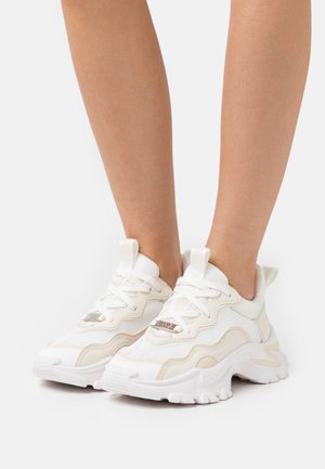 Białe siatkowe sneakersy z teksturowanymi detalami, zaokrąglonymi podeszwami i sznurowadłami. Zawierają odblaskowy srebrny akcent na języku oraz wyściełany kołnierz.