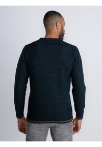 Marineblauer Strickpullover mit rundem Ausschnitt, gerippten Manschetten und einem braunen Akzent am Saum. Die Struktur des Stoffes ist durchgängig sichtbar.