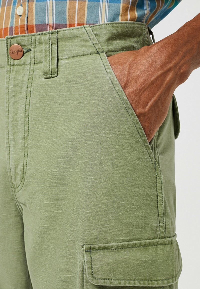 Pantalones cargo verde oliva con bolsillos laterales, con un corte recto y una textura sutil. El cierre con botón en la cintura añade un detalle.