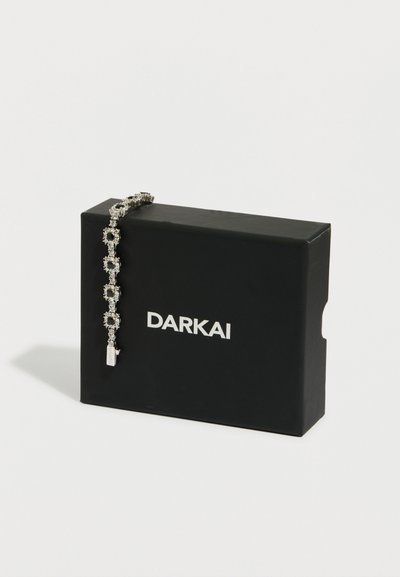 Ασημένιο βραχιόλι με τετράγωνα κρύσταλλα, τοποθετημένο πάνω σε μαύρο ορθογώνιο κουτί με την ετικέτα "DARKAI", σε λευκό φόντο.