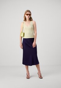 Lysegrønn ribbestrikket tanktop, marineblå midi-skjørt, svarte spissede hæler og en liten pastellgrønn håndveske. Brune solbriller fullfører stilen.