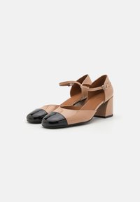 Pantofi din piele sintetică bej cu vârf din piele sintetică neagră. Au un toc pătrat și o curea la gleznă cu un cataramă argintie.