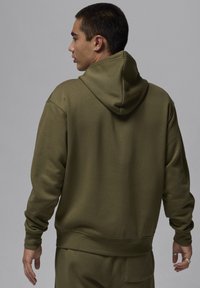 Felpa verde oliva con grande cappuccio, polsini e orlo a coste, texture liscia e vestibilità rilassata, vista da dietro.