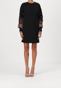 Svart klänning med rund halsringning och långa ärmar, med färgglad blomsterbroderi och rhinestones på ärmarna.